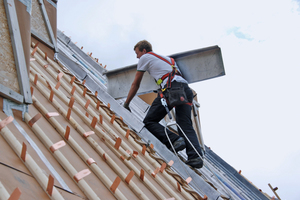  Ein angeseilter Handwerker bewegt sich auf dem sehr steilen Steildach 
 