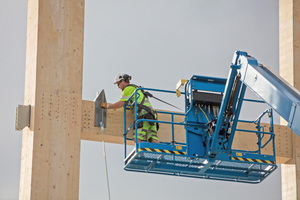  Ein Arbeiter verschraubt große Stahlplatten für die Aufnahmen von Querstreben an der Holzkonstruktion Foto: Moelven  