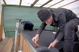  Holger Längle drückt die Plane mit der Anpresswalze an die Dachkante, der Kontaktkleber verbindet sich dadurch mit dem gekanteten Ablaufblech Foto: Rüdiger Sinn 