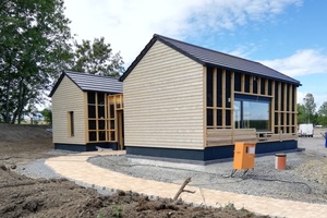  An der Giebelseite sind die Häuser bereits verschalt. An der Längsseite ist die Holzfassade noch in Arbeit 