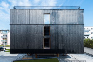  Das markante Erscheinungsbild der modernen Fassade prägen rauchschwarze Profile. Zudem steht der vierstöckige Holzbau auf Stelzen 