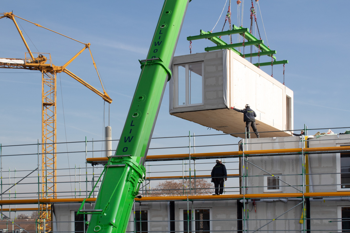 Holzmodulbauweise Holzmodulbau - Ein grüner Kran hebt ein Fertigmodul