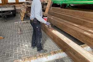  In der Werkshalle der Zimmerei werden Holzbalken für den Außenbereich mit einer 3-in-1-Holzschutzlasur beschichtet 