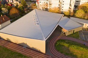  Das große Hallendach gliedert sich in zwei dreieckige Flächen. Der konkav gewölbte First verläuft von einem Eckpunkt der Halle zum schräg gegenüberliegenden Punkt 