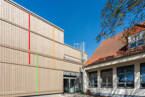  Der Neubau mit Holzfassade wurde an das bestehende Schulgebäude (rechts im Bild) angebaut. Die Anbindung des Neubaus an die bestehenden Gebäude erfolgte durch mehrere Übergänge 