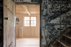  Blick vom historischen Bestand in den lichtdurchfluteten Neubau: Der starke Kontrast zwischen dunklem, gealtertem Holz und hellen, klaren Oberflächen unterstreicht den Dialog zwischen Alt und Neu im Museum Bezau 