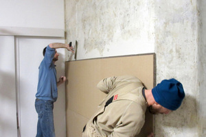  Ein Handwerker drückt die Platte an die Wand, während der zweite schon neuen Spachtel für die nächste Platte aufzieht 